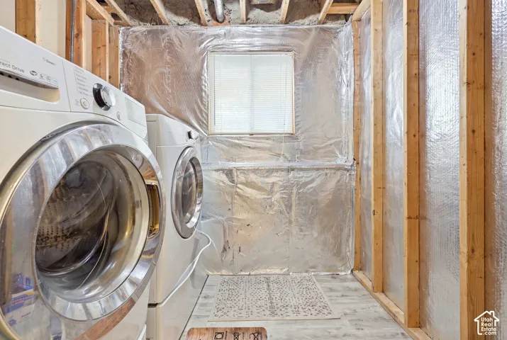 Utility space featuring exposed wood-stud framing, reflective foil insulation, a single-pane window with blinds, and light-toned wood-finish flooring