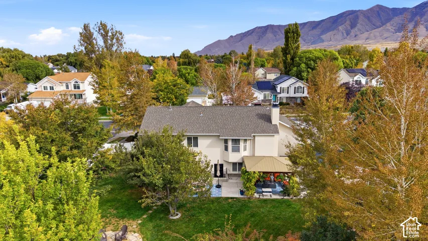 Aerial perspective of a multi-level residence featuring a covered patio, a masonry chimney, expansive lawn, and a backdrop of mountain scenery