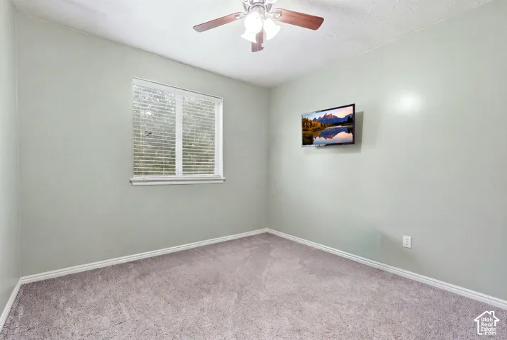 Neutral-toned wall paint, neutral carpeting, single-hung window with white shutters, and a central ceiling fan with an integrated light fixture