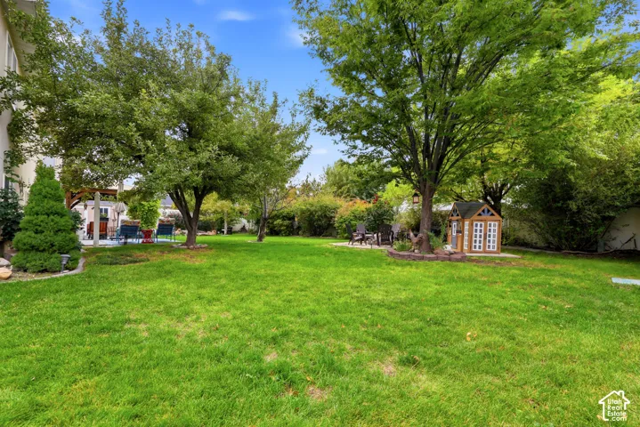 Expansive backyard featuring a manicured lawn, mature trees, concrete patio space, and stone landscaping borders