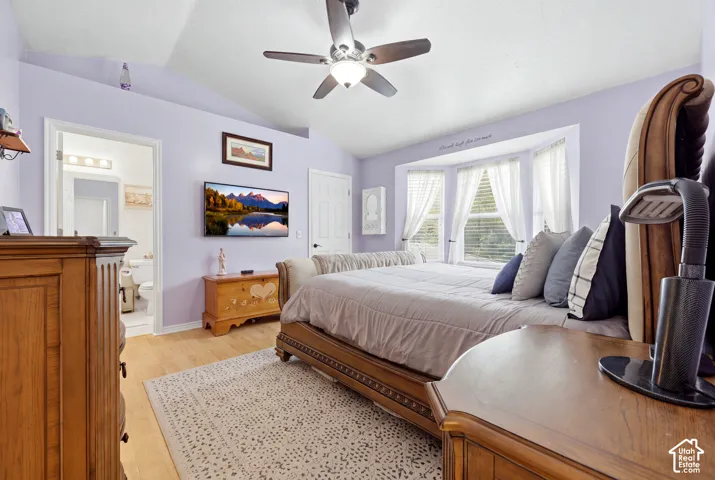 Vaulted ceiling with a central multi-blade ceiling fan, bay window, and wood-finish flooring