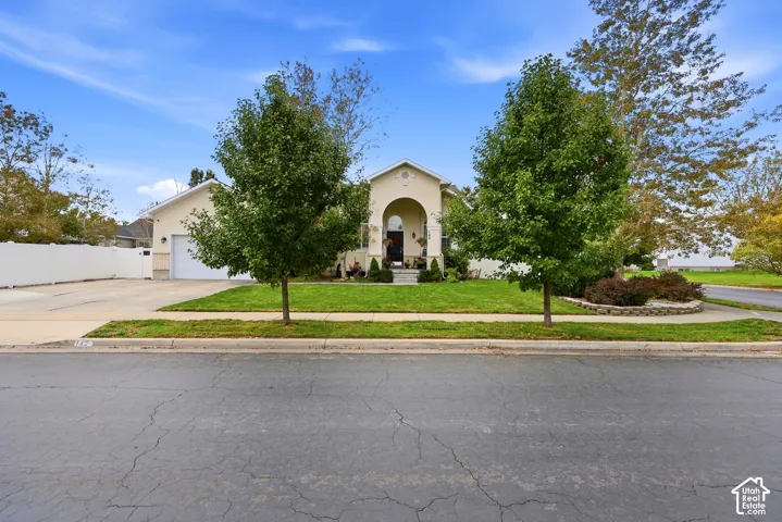 Stucco exterior featuring an arched entryway, gabled roofline, concrete driveway, and white vinyl perimeter fencing