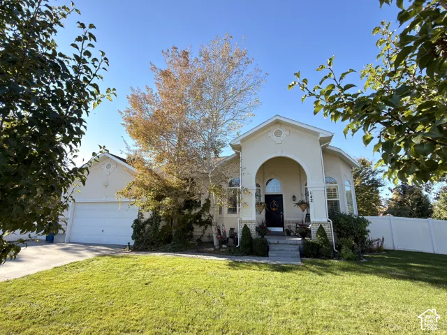 Stucco exterior featuring an arched entryway, stone-accented foundation, multi-pane windows with arched transoms, and a two-car garage