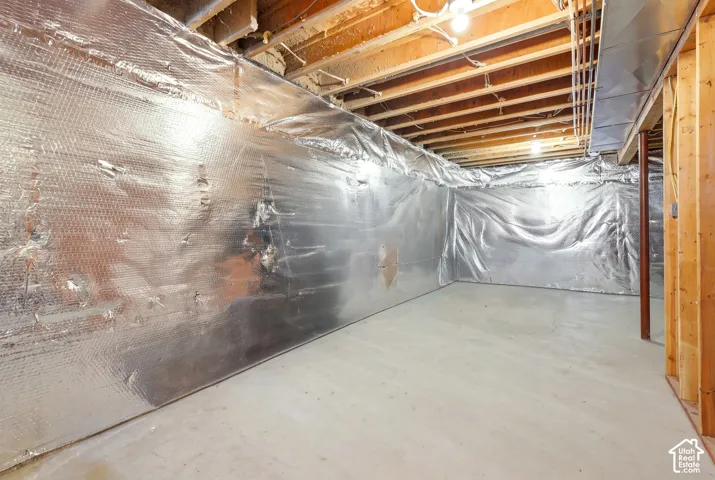 Unfinished basement space featuring exposed wooden floor joists, reflective radiant barrier wall insulation, a concrete floor, and structural support columns
