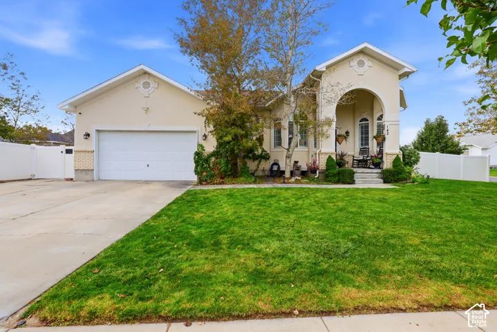 Stucco exterior featuring an arched covered porch, two-car garage, stone masonry accents, and vinyl perimeter fencing