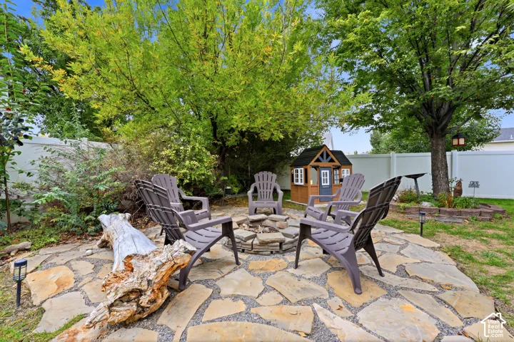 Backyard featuring a flagstone patio, stone fire pit, white vinyl fencing, and mature trees