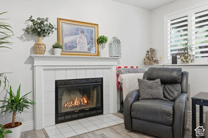 Fireplace featuring a white mantel, square tile surround, and wood-finish flooring, accented by shutter-style window coverings