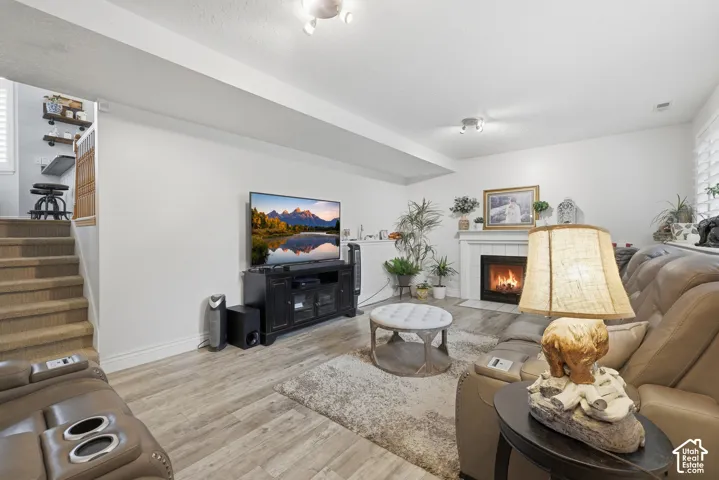 Living area featuring wood-finish flooring, a white-mantel fireplace, recessed ceiling lighting, and carpeted stairs