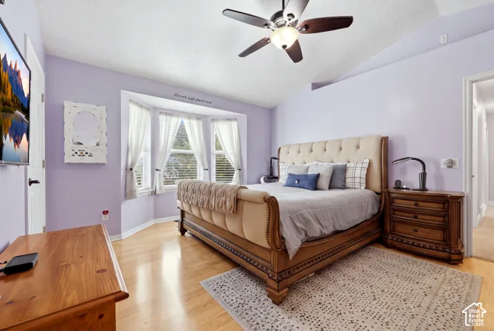 Vaulted ceilings, bay window, and wood-finish flooring with a central ceiling fan and light fixture