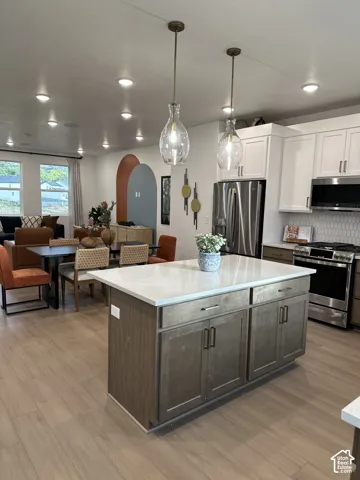 Kitchen featuring a central island with a solid-surface countertop, wood-finish cabinetry, stainless steel appliances, recessed ceiling lighting, and pendant fixtures