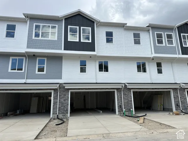 Multi-level townhouse exterior featuring stacked stone veneer, horizontal lap siding, shingle-style siding accents, and multiple attached garage bays