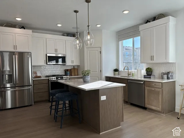Kitchen featuring two-tone shaker cabinetry, quartz countertops, hexagonal tile backsplash, stainless steel appliances, and pendant lighting