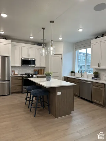Kitchen featuring two-tone cabinetry, central island with stone-surface countertop, stainless steel appliances, geometric tile backsplash, and wood-finish flooring