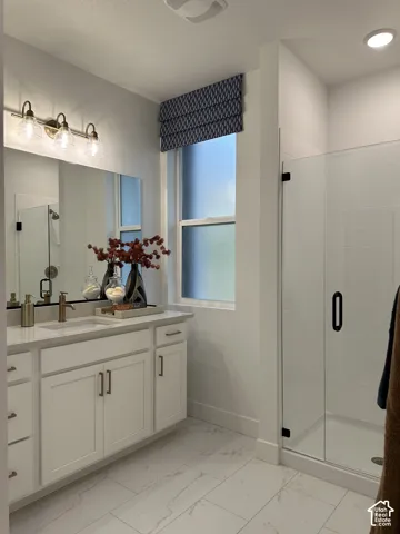 Bathroom featuring a white shaker-style vanity with stone-finish countertop, under-mount sink, brass-tone hardware, and a frameless glass-enclosed shower with tile surround