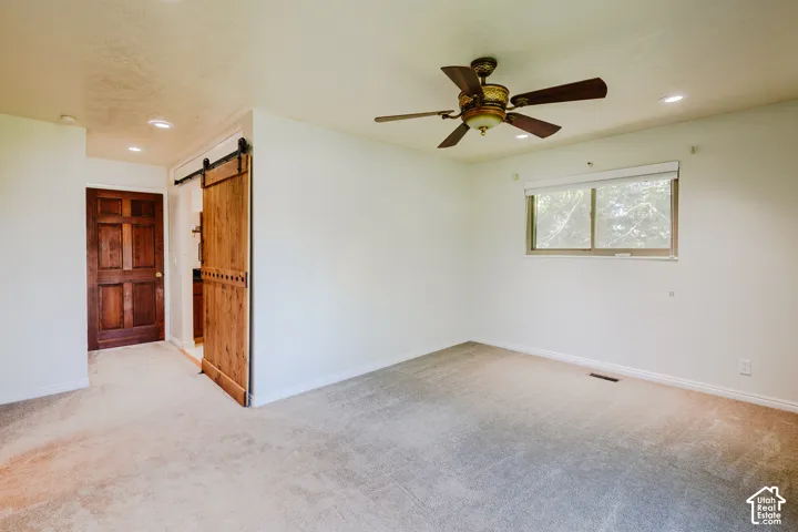 Interior space featuring a sliding wood barn door, recessed lighting, ceiling fan, neutral carpeting, and a six-panel wood door