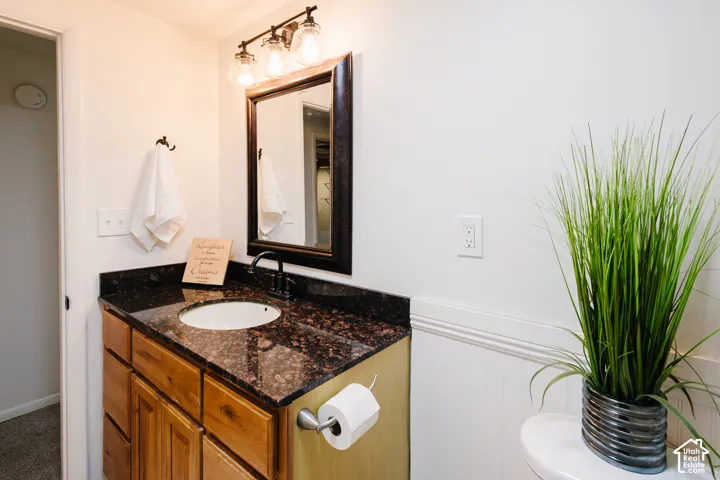 Natural wood vanity featuring a stone countertop with an integrated basin, dark metal faucet, framed mirror, and three-light wall-mounted fixture