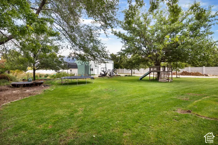 Expansive backyard featuring a large grass lawn, mature shade trees, a concrete block perimeter wall, and a detached metal workshop