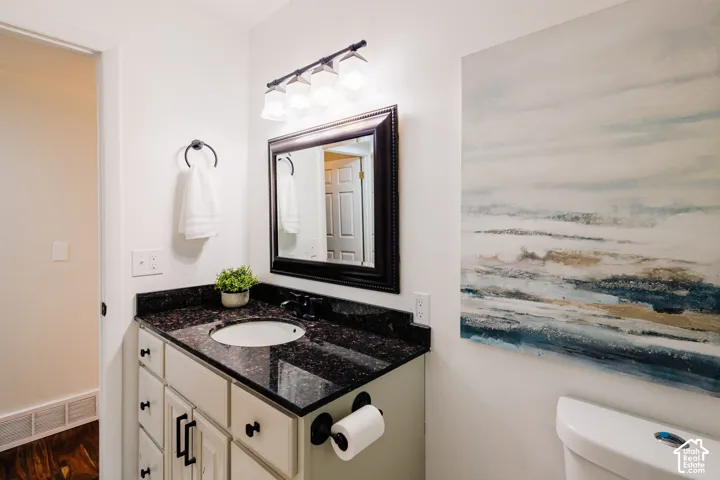 Bathroom featuring a vanity with dark stone countertop, integrated undermount sink, dark-finished hardware, framed mirror, and four-light fixture