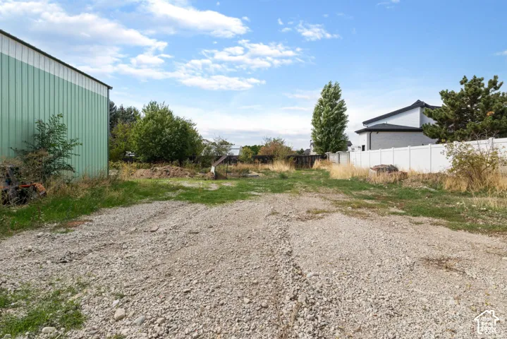 Expansive level lot featuring a detached metal structure, gravel surface, and vinyl privacy fencing