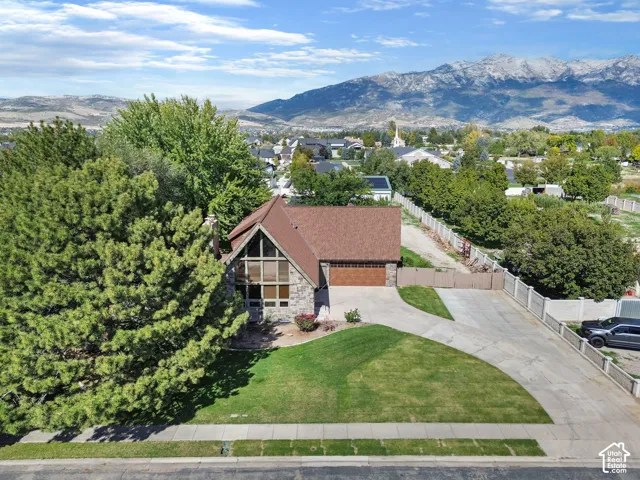 A-frame architectural exterior featuring multi-story windows, stone facade, asphalt shingle roofing, attached two-car garage, and mountain backdrop