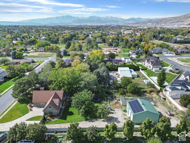 Aerial perspective featuring a multi-level residence with an attached garage, a detached workshop with roof-mounted solar panels, mature landscaping, and mountain backdrop