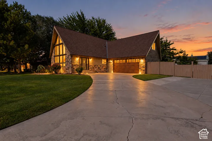 A-frame style exterior featuring stone masonry cladding, multi-pane floor-to-ceiling windows, an attached two-car garage, and an expansive concrete driveway