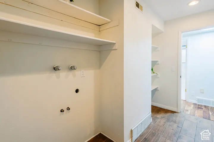 Utility space featuring wood-finish flooring, white built-in shelving, and dedicated water and electrical hookups
