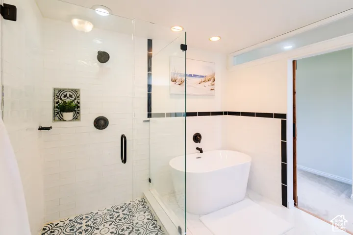 Walk-in glass shower with matte black fixtures, white subway tile surround, patterned tile floor accent, and freestanding soaking tub
