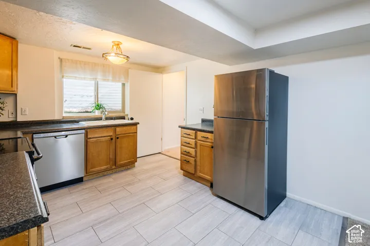 Kitchen featuring stainless steel appliances, wood cabinetry, tile flooring, and a drop-in sink