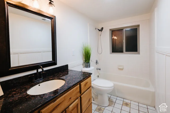 Bathroom featuring a wood vanity with a dark stone countertop, an undermount oval sink, a framed mirror with integrated lighting, and a combination tub and shower with tile surround