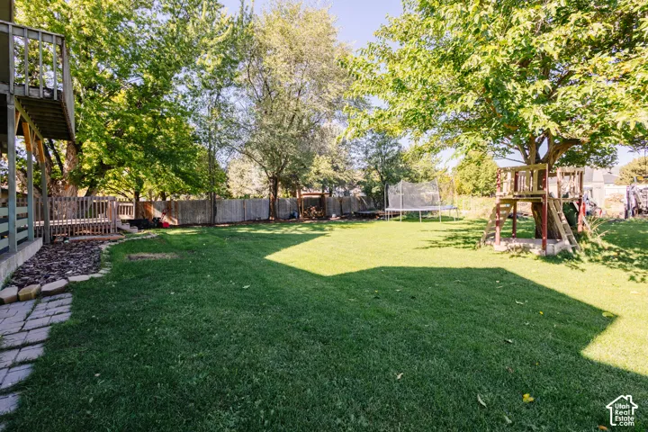 Expansive backyard featuring a large grass lawn, mature trees, wood privacy fencing, and a raised wooden deck