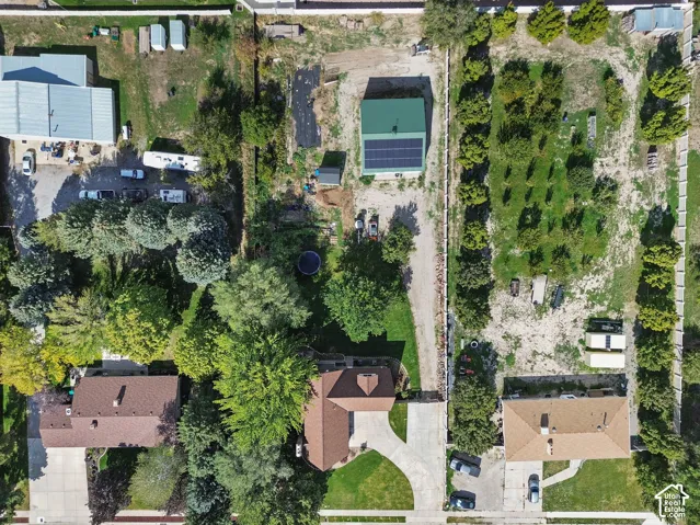 Aerial perspective of a sprawling lot featuring mature trees, an expansive open lawn, an attached garage, and a detached outbuilding equipped with roof-mounted solar panels