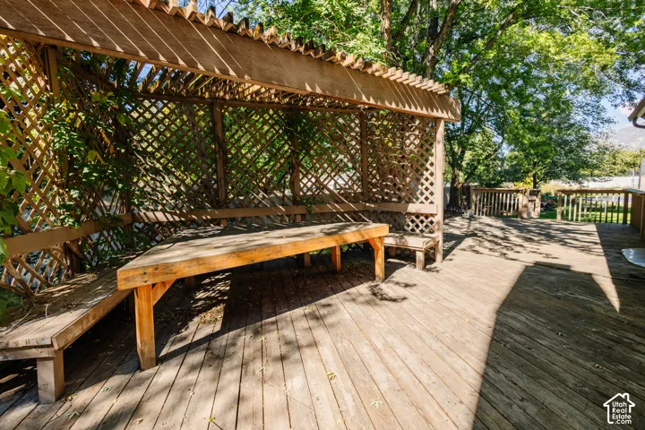 Wooden deck featuring an attached wood-lattice pergola and integrated wood bench seating
