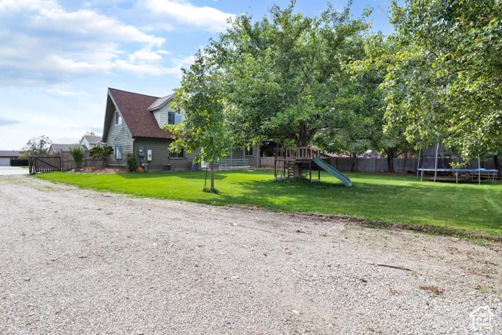 Expansive lawn featuring mature trees, wood-sided exterior, steep-pitch roofline, and gravel driveway