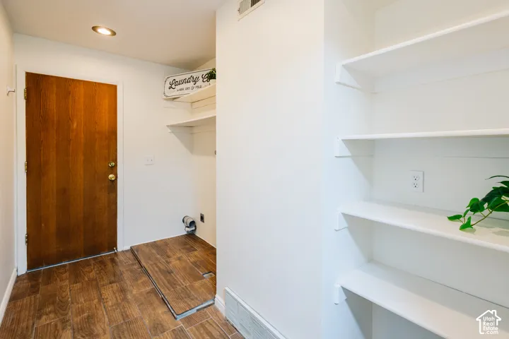 Utility area featuring wood-finish tile flooring, recessed lighting, built-in white shelving, and a solid wood entry door