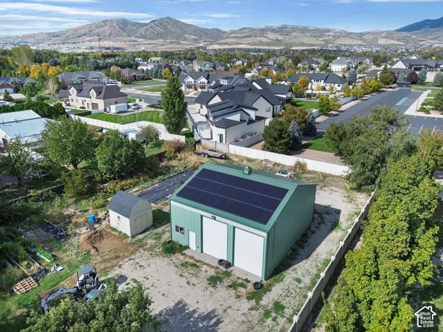 Detached metal-sided structure featuring dual garage doors, solar panel array, and a secondary storage shed, situated on a parcel with mountain backdrop