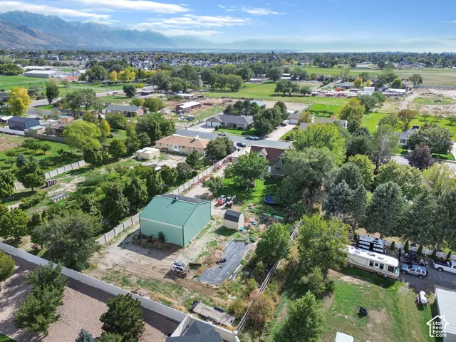 Aerial perspective featuring a detached metal structure, expansive grounds with mature trees, perimeter fencing, and a mountain backdrop