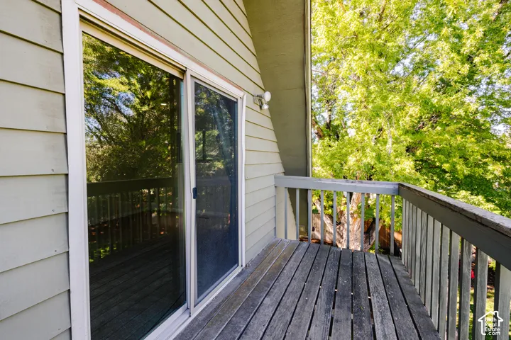 Exterior balcony featuring wood decking, wood-frame railings, horizontal lap siding, a glass sliding door, and wall-mounted exterior lighting
