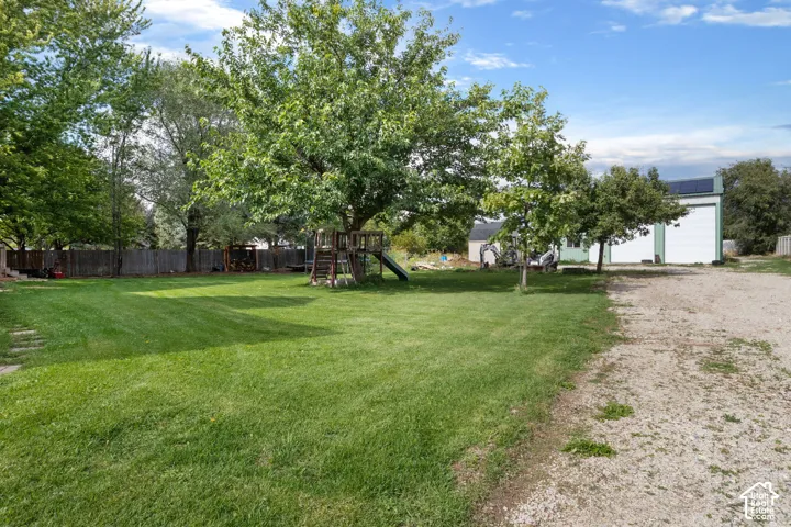 Expansive grounds featuring a manicured lawn, mature trees, wood fencing, and a detached multi-bay structure with rooftop solar panels