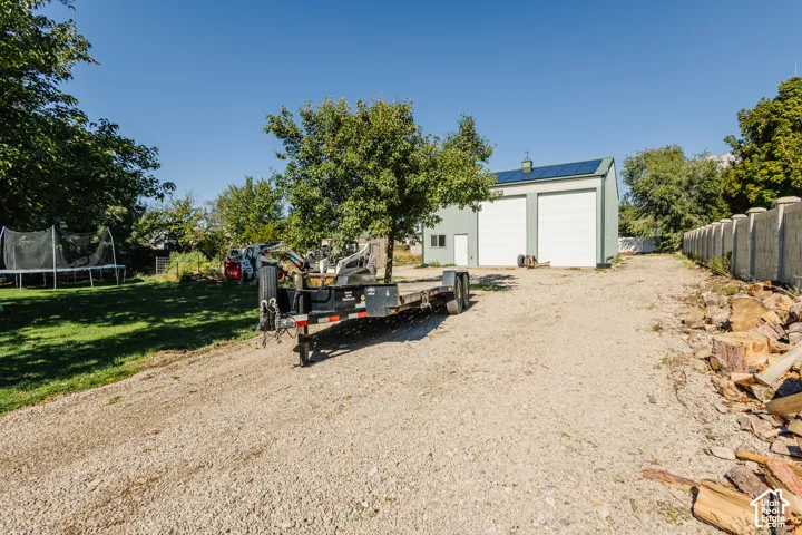 Detached metal-sided structure featuring dual garage doors and rooftop solar panels, situated on a lot with an extensive gravel driveway and perimeter wall
