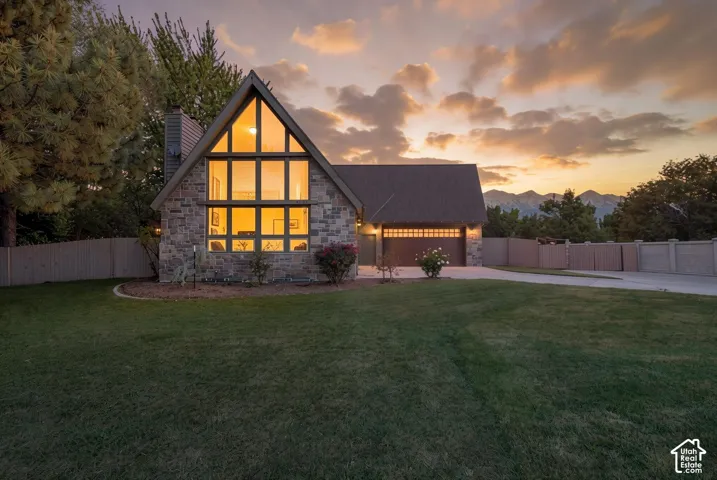A-frame architecture featuring stone exterior siding, multi-pane floor-to-ceiling windows, an attached two-car garage, and mountain scenery