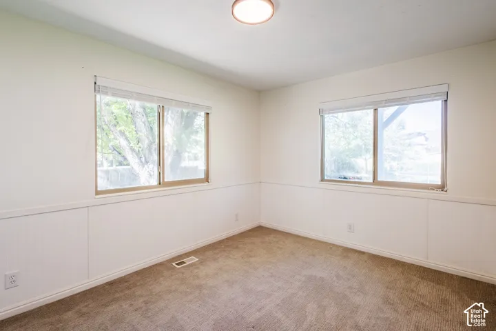 Room featuring white beadboard wainscoting, neutral carpeting, and two dual-pane sliding windows with integrated blinds