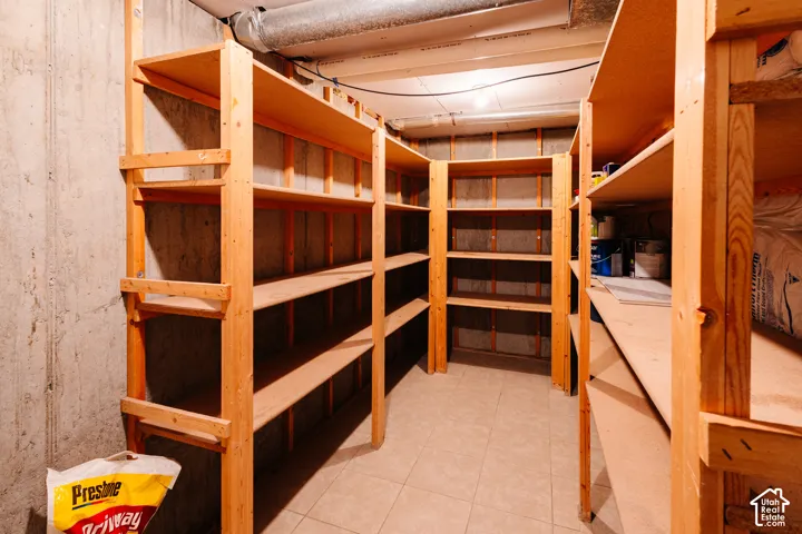 Storage area featuring floor-to-ceiling wooden shelving units, concrete walls, and tile flooring