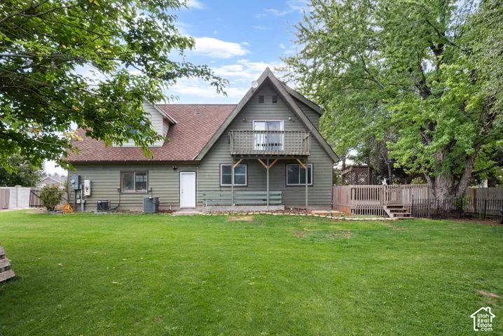 Exterior featuring green siding, a second-story balcony, a wooden deck, and mature trees on a lawn