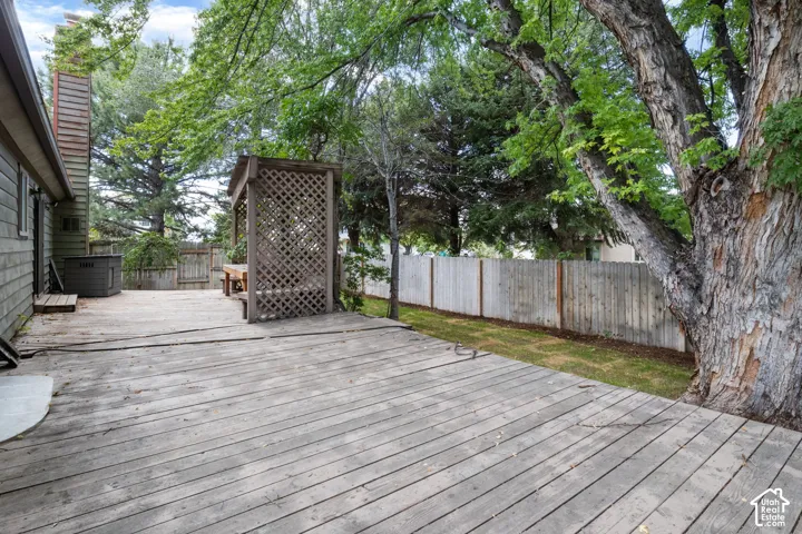 Rear exterior featuring an expansive wood deck, built-in wooden lattice pergola, horizontal wood fence, and mature trees