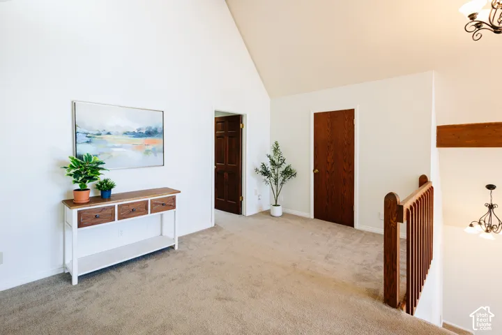 Vaulted ceilings, neutral carpeting, and a wooden balustrade with a stained-wood railing