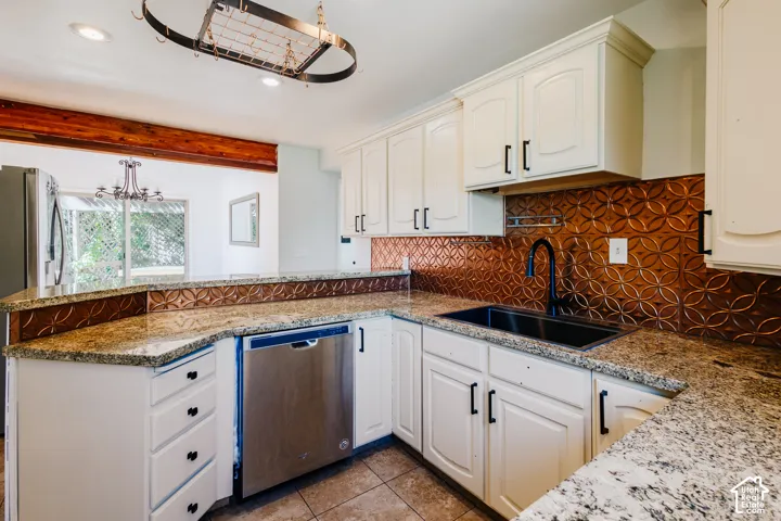 Kitchen featuring light-toned cabinetry, stone countertops, textured metal backsplash, under-mount sink with matte black faucet, and suspended overhead pot rack