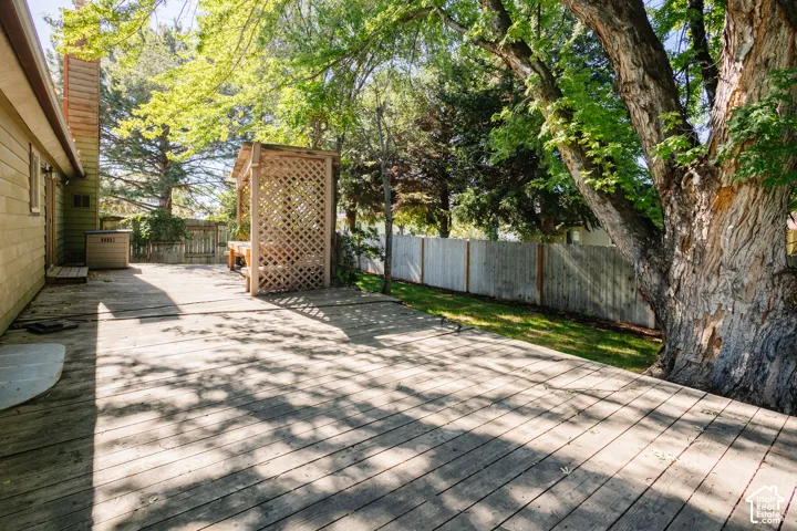 Expansive wood deck featuring a lattice-enclosed pergola, mature shade trees, and a vertical wood privacy fence