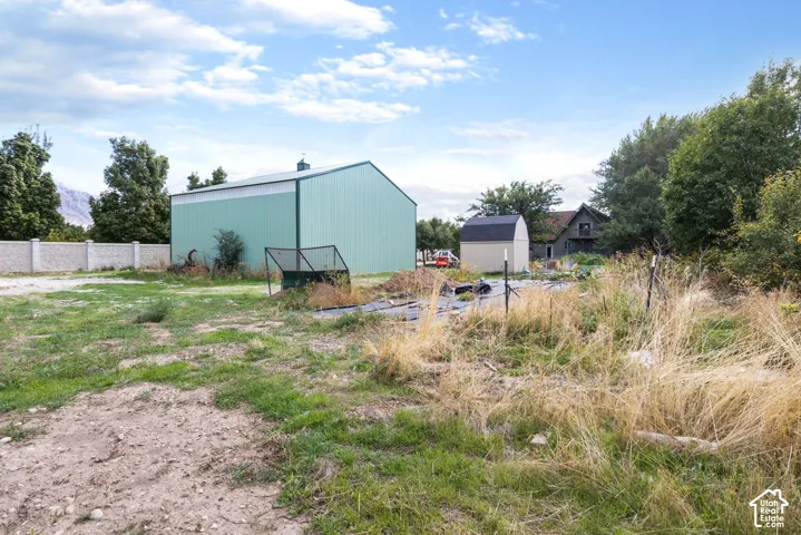 Expansive grounds featuring a metal-sided workshop, a detached shed, perimeter fencing, and mature trees