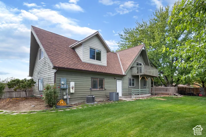 Exterior featuring horizontal siding, a steeply pitched shingled roof, a second-story wooden balcony, and an expansive lawn